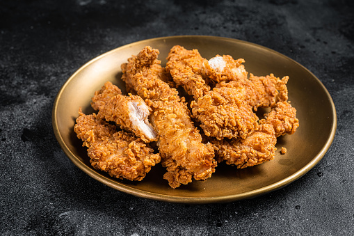 Breaded chicken strips, breast fillet meat on a plate. Black backgrund. Top view.