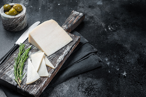 Dutch goat cheese sliced on a wooden cutting board. Black background. Top view. Copy space.