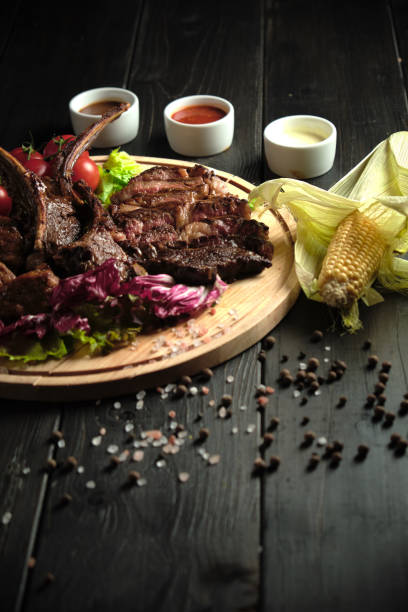 Meat on the bone on a wooden board with different sauces on a dark wooden background catering menu