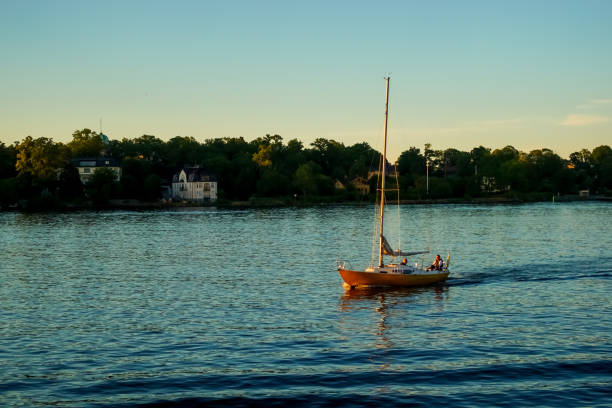 Yellow small sailboat cruising on calm water with engine to harbor on a summer evening in the Stockholm archipelago
