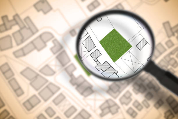 istock Imaginary cadastral map of territory with a free green land available for building construction. Concept image with buildings and roads through magnifying glass 1409647340