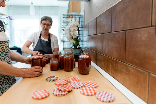 Senior Mother and Mature Daughter in Domestic Kitchen Canning in Jars Traditional Homemade Apricot Jam