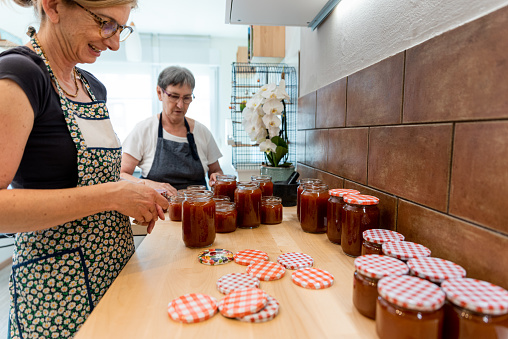Senior Mother and Mature Daughter in Domestic Kitchen Canning in Jars Traditional Homemade Apricot Jam