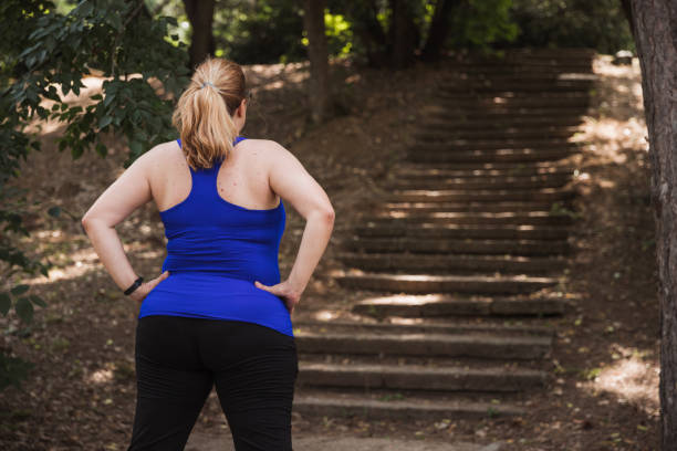 Rear view of a woman standing in front of stairs in the park Woman holding hands on hips when observing stairs in a park that she was about to run on runner on start pose stock pictures, royalty-free photos & images