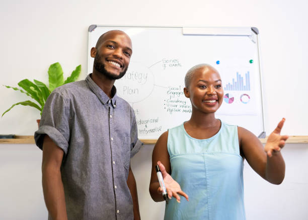 istock Two Black coworkers give a presentation in an office with whiteboard 1409649130