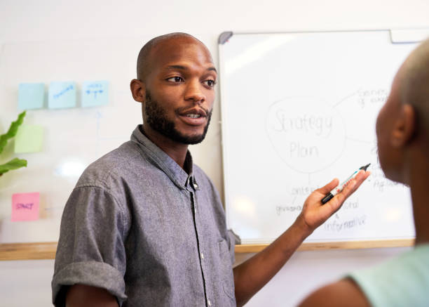 istock A Black businessman discusses strategy with coworker gesturing to whiteboard 1409649370