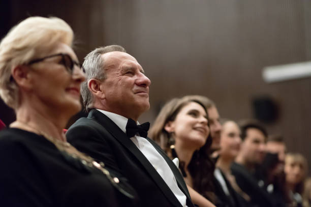 Side view of happy multi ethnic audience sitting in the opera. Men and women are watching theatrical performance. They are in elegant wear.