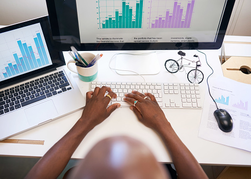 An overhead view of man typing report with graphs at desk with two screens. High quality photo