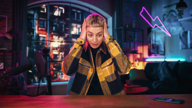 istock Ecstatic Young Female with Short Hair Talking Into Microphone While Recording Podcast from Loft Apartment. Happy Surprised Woman Talking on Camera and Recording Radio Show Live on Social Media. 1409652359