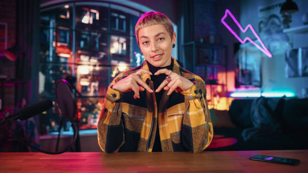 istock Attractive Young Female Talking Into Microphone While Recording Radio Show from Her Loft Apartment. Happy Woman with Short Hair Talking on Camera and Recording Podcast Live on Social Media. 1409652543