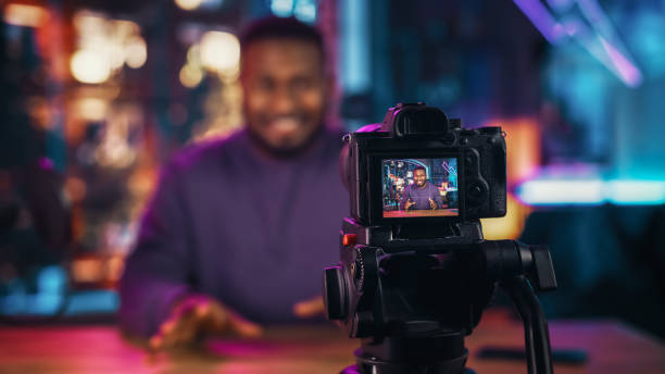 istock Handsome Young African American Man Talking Into Microphone While Recording Radio Show from His Loft Apartment. Happy Black Male Talking on Camera and Recording Podcast Live on Social Media. 1409652731