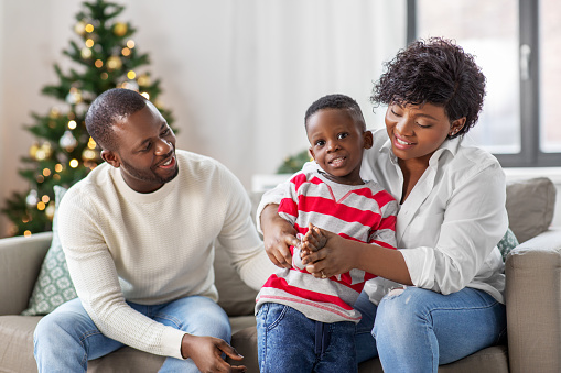 family, winter holidays and people concept - happy african american mother, father and baby son at home on christmas