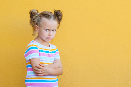 Serious pensive little kid girl looking unhappy at camera, upset preschool child melancholic or bored, isolated over yellow studio background