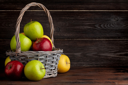 Colorful ripe apple fruits in basket on wooden table. With copy space