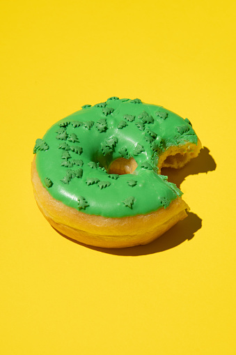 Bitten donut in green on a yellow background, vertical, studio photo.