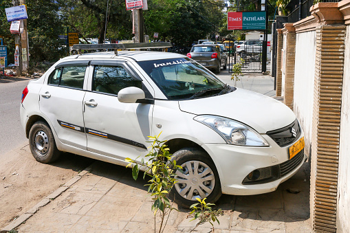 Gurgaon, India - March 4, 2022: White compact car Maruti Suzuki Swift DZire in the city street.