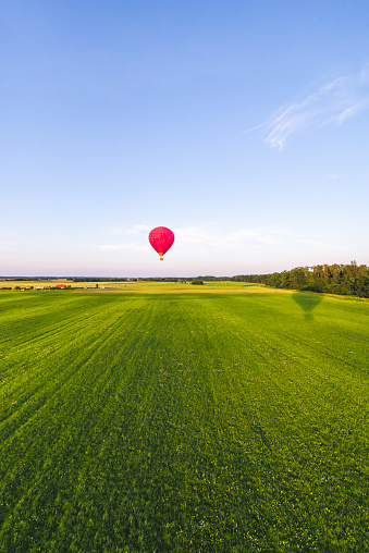 Flying with hot air balloon over field of rye in the evening, clear blue sky.