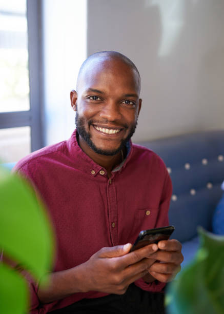 istock An attractive Black man smiles at the camera while using his phone 1409665598