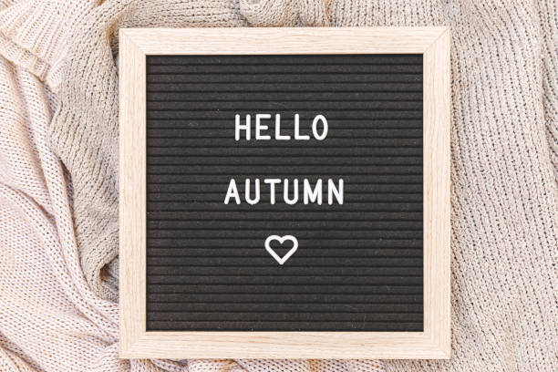 istock Autumnal Background. Black letter board with text phrase Hello Autumn lying on white knitted sweater. Top view, flat lay. Thanksgiving banner. Hygge mood cold weather concept 1409666534