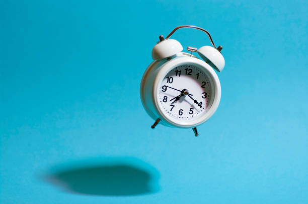 istock White retro style alarm clock flying on blue background throwing hard shadow. Flying analog clock. 1409667576