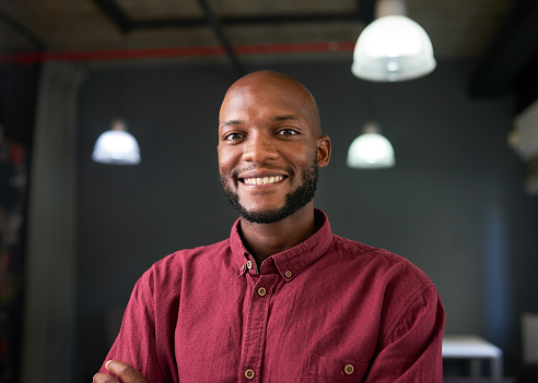 A confident happy Black man poses in red shirt in an industrial office. High quality photo