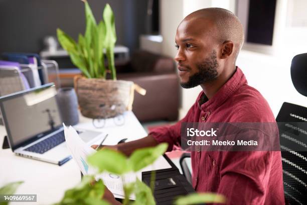 A Black man sits at his office desk with notes and laptop