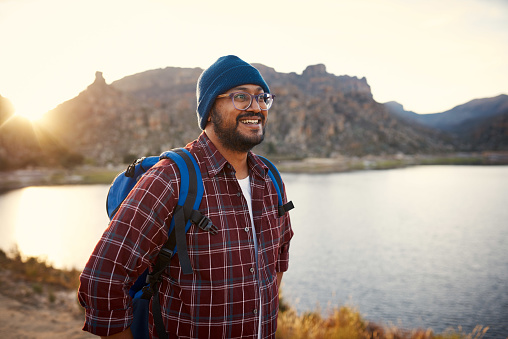 A young adult backpacker smiles at the lake view with sunset behind him in the mountains . High quality photo