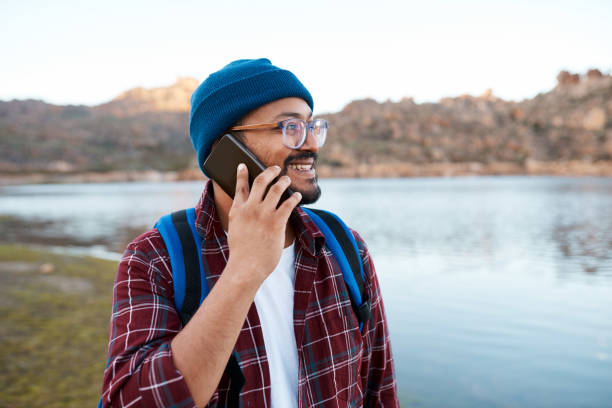 A man makes a call on smartphone while hiking in the mountains at a lakeside. High quality photo