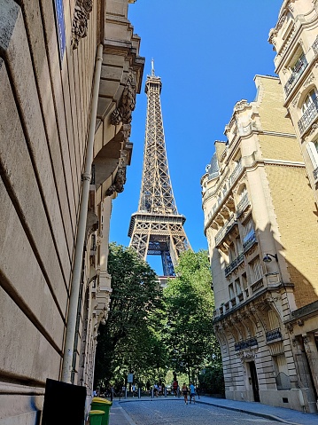 Eiffel Tower, Paris, view from a side street with facades of old traditional buildings and branches of a tree in the forefront during daylight with cloudy sky in the background, no people, low angle view, horizontal