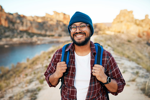 An attractive hiker smiles at the camera with backpack in the mountains at sunset. High quality photo