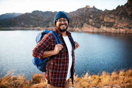 A happy hiker poses by the lakeside with backpack and beanie in the fall weather. High quality photo