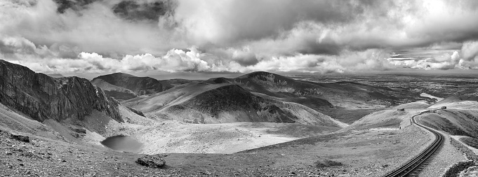 Panorama of the mountains of Snowdonia looking from Mount Snowdon, with a vintage steam train climbing from the town of LLanberis to the summit. Black and white version