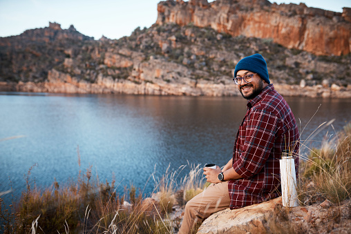 A man takes a break by the lakeside drinking coffee from a flask. High quality photo