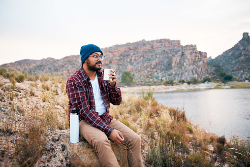 A young adult man takes a break from hiking drinks coffee by the lake view. High quality photo
