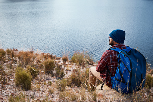 A backpacker takes a break and sits on a rock by the lake while hiking. High quality photo