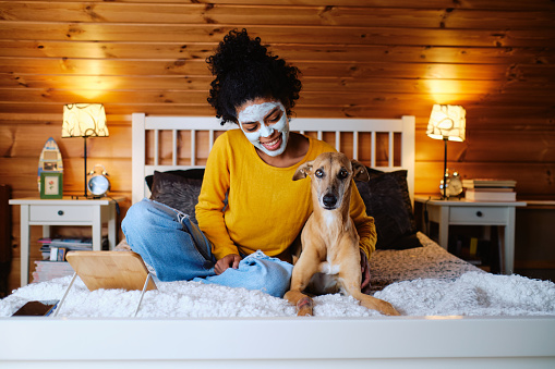 Sitting on the bed in her bedroom and happy for the company of her dog waiting to take off the face mask she is wearing.