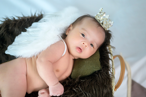 Rear view of sweet baby girl in an Angel costume sitting against a gray wall on a fluffy blanket.