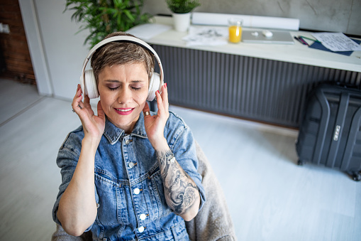 Shot of a mature woman sitting in her study listening to music through wireless headphones