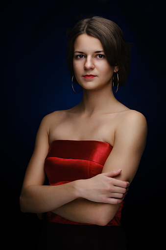 Studio shot of young serious caucasian transgender woman looking at camera with arms crossed on dark background