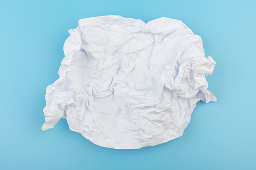 A piece of crumpled white paper on a blue background. Creativity crisis concept.