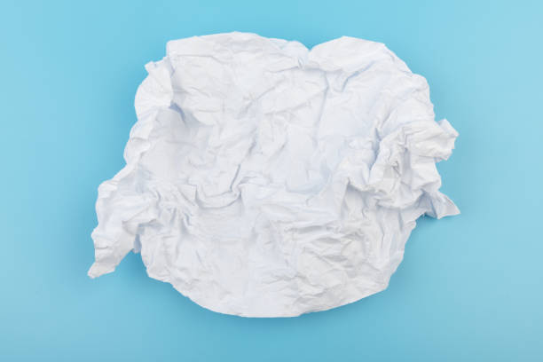 A piece of crumpled white paper on a blue background. A piece of crumpled white paper on a blue background. Creativity crisis concept. crumpled paper ball stock pictures, royalty-free photos & images