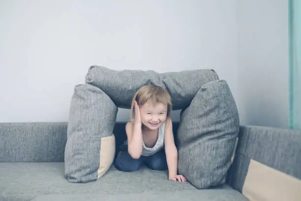 Photo of funny European child playing with pillows on couch