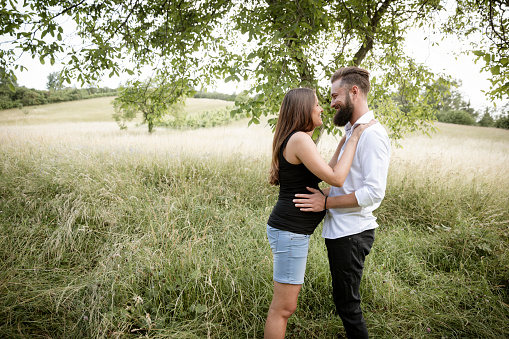 pretty young pregnant woman with black shirt is standing with her boyfriend in a high meadow and they are happy and full of anticipation for the baby