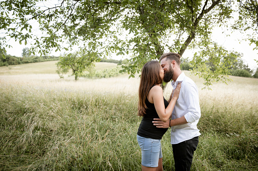 pretty young pregnant woman with black shirt is standing with her boyfriend in a high meadow and they are happy and full of anticipation for the baby