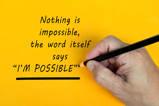 Male hand writes in black pencil the word NOTHING IS IMPOSSIBLE, THE WORD ITSELF SAYS I AM POSSIBLE on a yellow background.