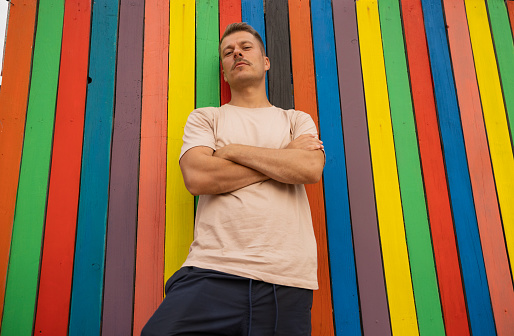 Portrait of a confident young Caucasian man with arms crossed, leaning on the multicolored wall of timbers