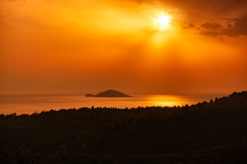 Orange/gold colored sky, during majestic sunset above the sea and mountain