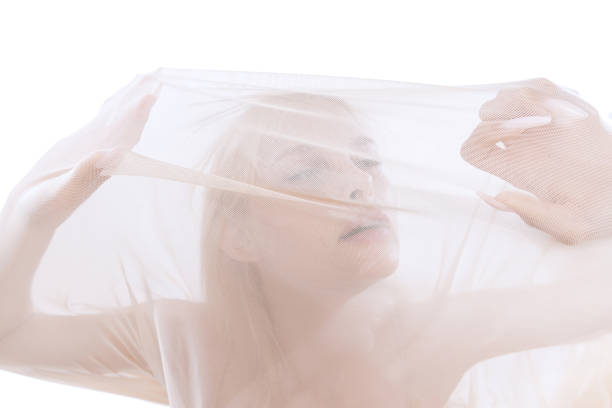 Pain, despair. Emotions, facial expression. Young tender beautiful girl under transparent fabric, cloth isolated on white studio background. Grace, art, beauty, ad concept. Monochrome. Closeup.