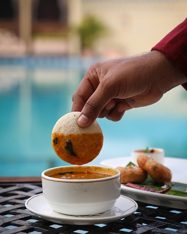 Idli dipped in sambhar with vada in background. Shot in front of pool.