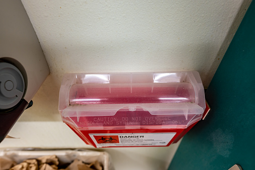 Red biohazard sharps waste container mounted to the wall of a public restroom. High quality photo